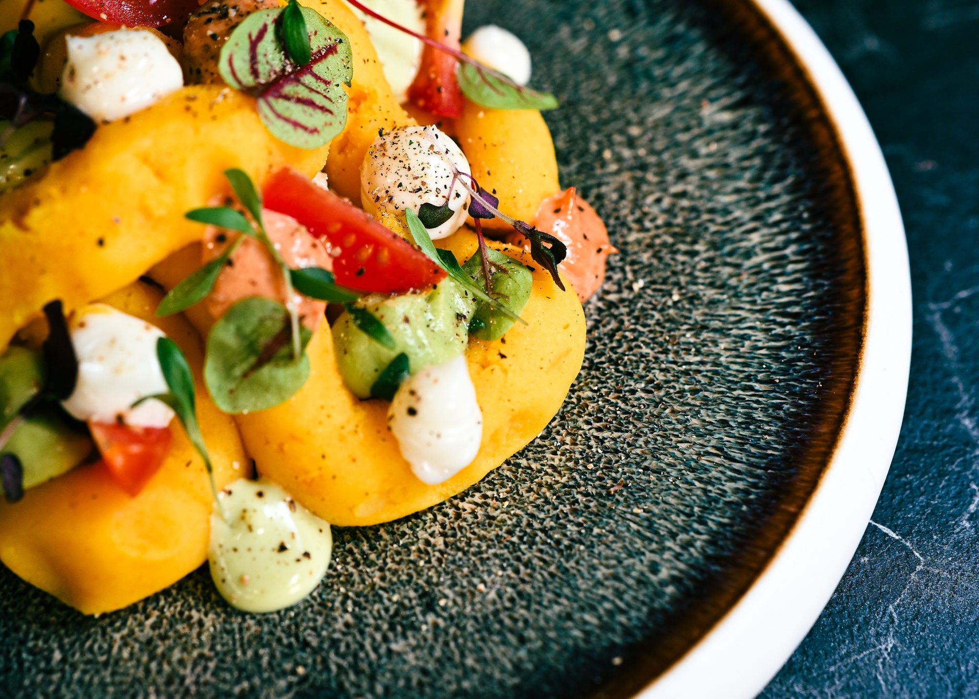 Causa de tourteau du Barranco : purée de pomme de terre à l’ají amarillo, tomate, avocat et pousses, servie sur une assiette sombre